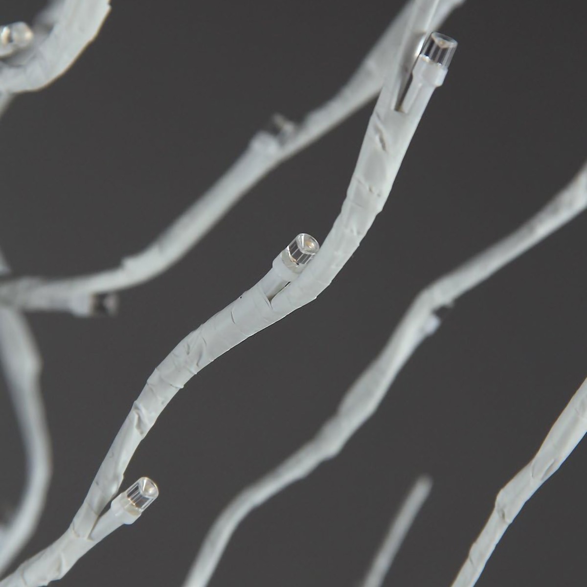 Gałęzie drzewka w kolorze białym, z widoczną fakturą przypominającą korę brzozy, a wzdłuż nich umieszczone  małe, ciepłe diody LED, które emitują światło. Na ciemnym tle. 